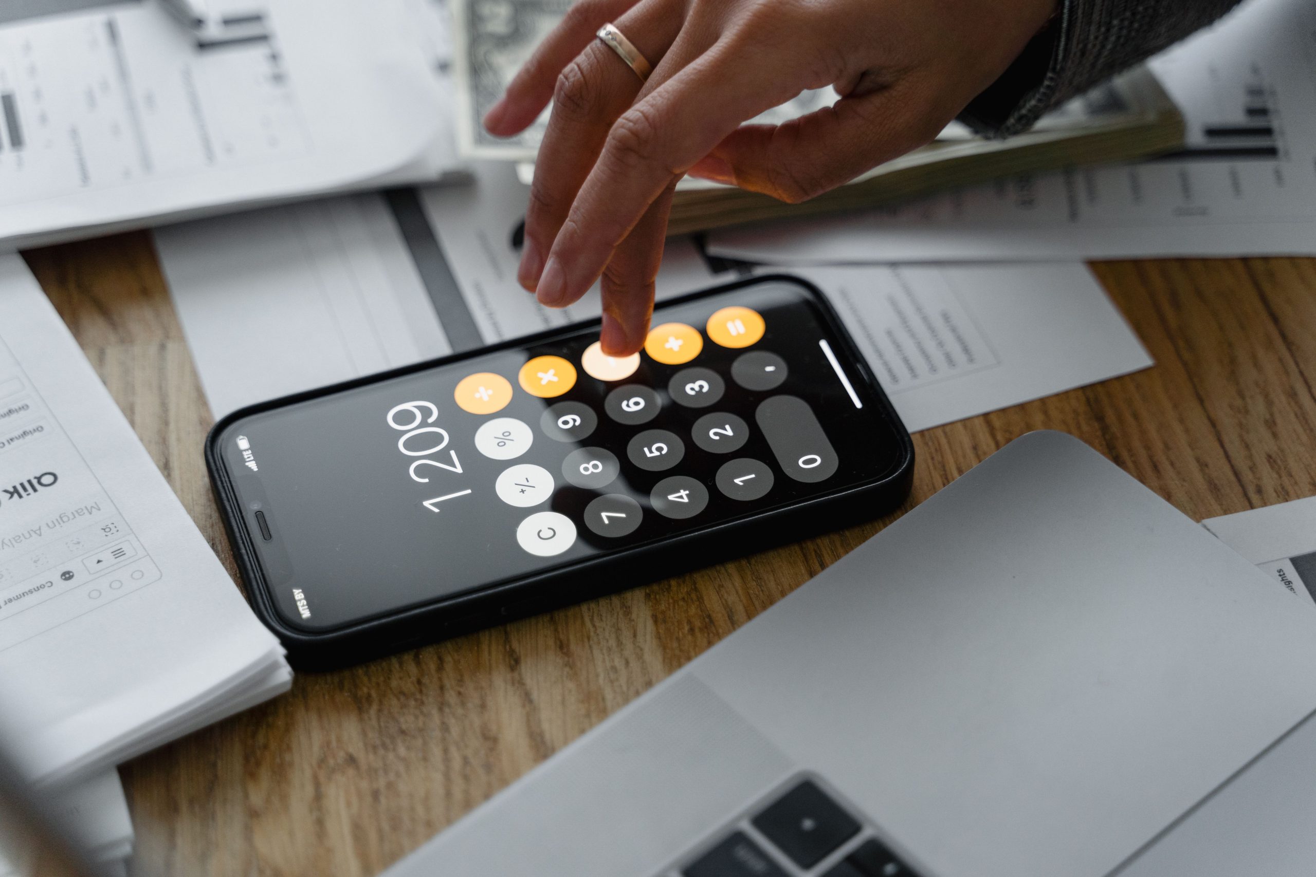 Person using a calculator beside business documents while reviewing operating expenses