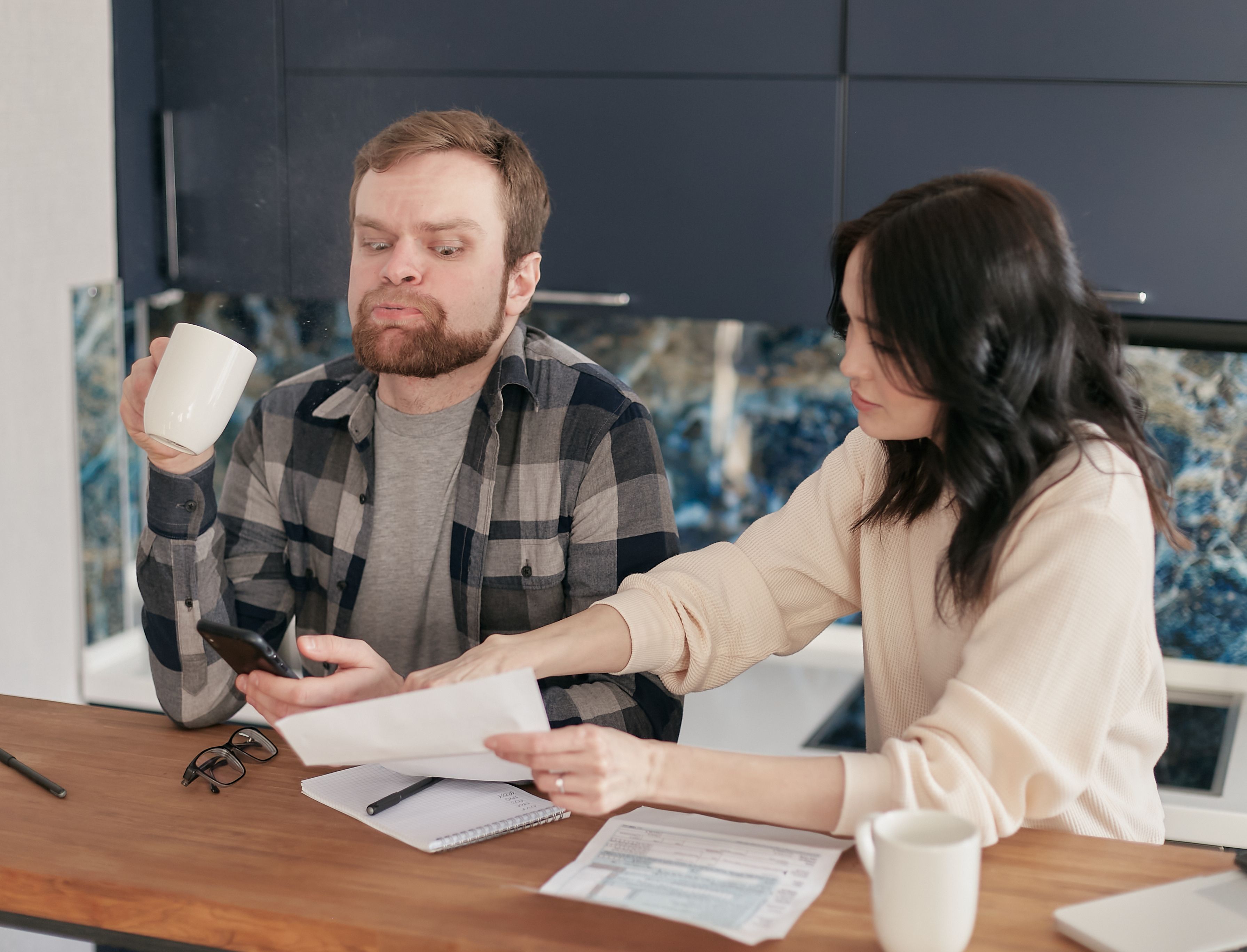 A couple looking worried while reviewing household bills at their kitchen table, reflecting cost of living concerns.